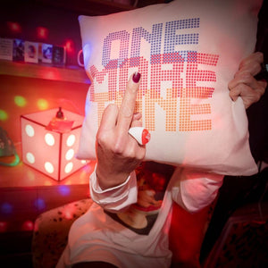 Photo of woman giving us the middle finger from behind a funky Famous Rebel cushion.