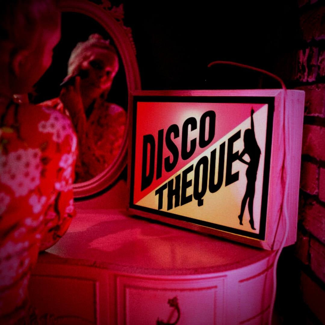 A Discotheque light box sign on a dressing table next to a woman doing her make-up.