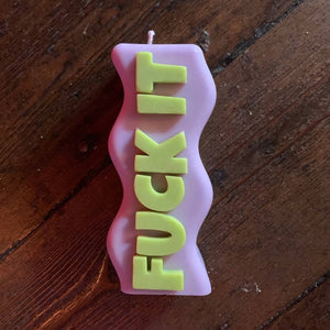 A pink candle with the words Fuck It on it in yellow